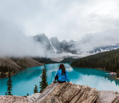 Person overlooking a serene turquoise lake surrounded by misty mountain