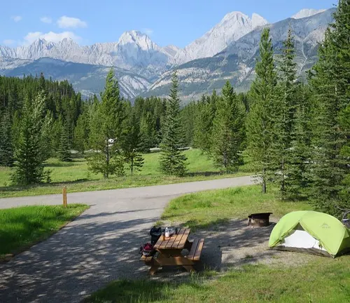 Serene campsite with a tent and picnic table surrounded by lush greenery and mountains