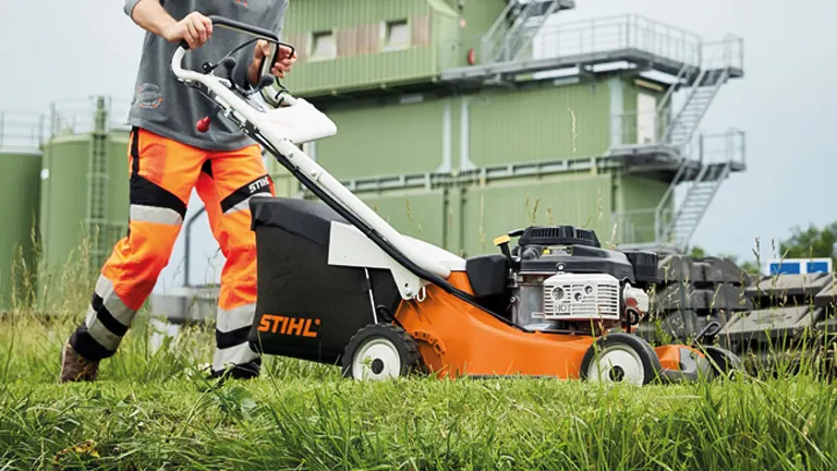 Person using a STIHL RM 756 YC lawn mower on tall grass in an industrial setting