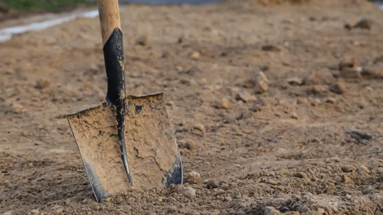 A shovel embedded in a mound of freshly tilled soil.
