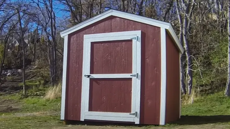A small, freshly painted red shed with white trim, located in a wooded area.

