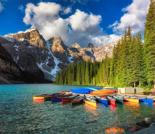 Colorful canoes on a clear lake with rocky mountains and green trees at Banff National Park