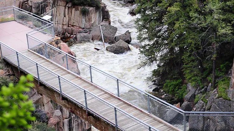 Metal walkway bridge over a rocky, fast-flowing river in Bighorn Scenic Byway