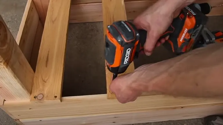 Close-up of a person using a power drill to secure wooden beams in a frame.