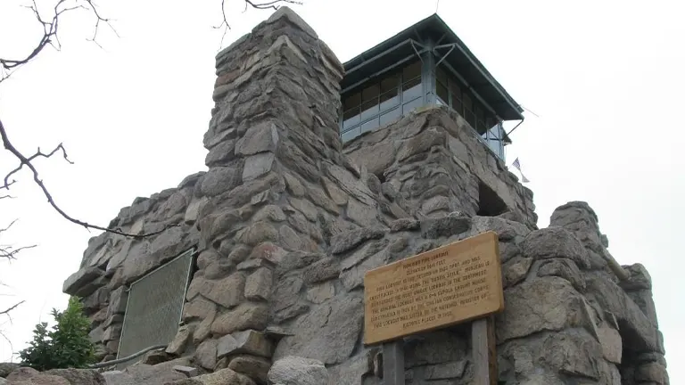 a stone lookout tower located in Lincoln National Forest. The tower, constructed from large, rough stones, has a small windowed enclosure at the top