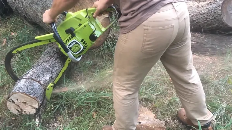 individual using a bright green bow saw chainsaw to cut through a large log, with wood chips flying away from the cutting site