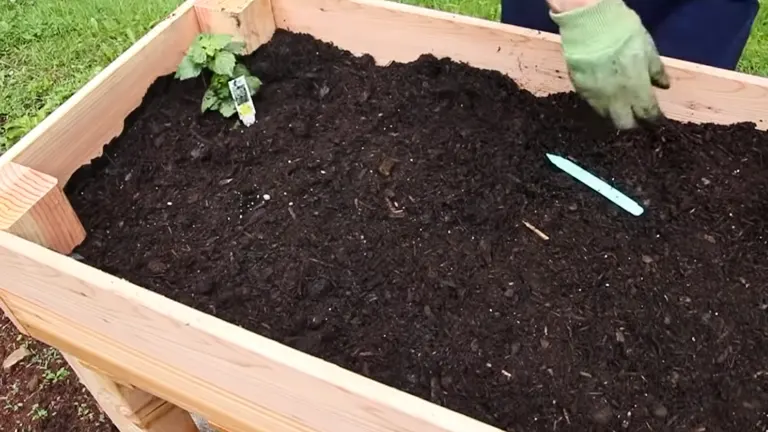 A person spreading soil in a nearly completed wooden raised garden bed outdoors.