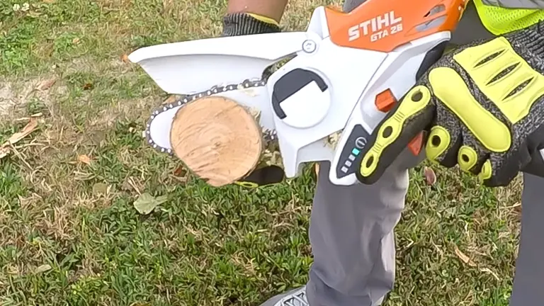 Person holding a STIHL GTA 26 mini chainsaw cutting a small log