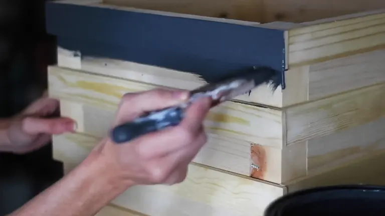 A hand using pliers to paint or apply finish to a small wooden box.