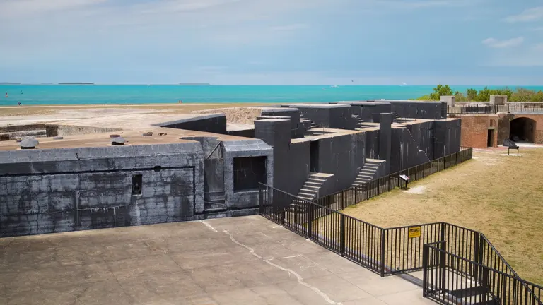 A view of the historic Fort Zachary Taylor with its dark, aged walls and staircases, overlooking a bright blue sea under a clear sky