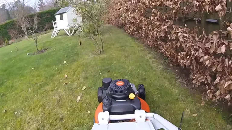 STIHL RM 756 YC lawn mower in action, cutting grass near a leafy hedge and a small white playhouse
