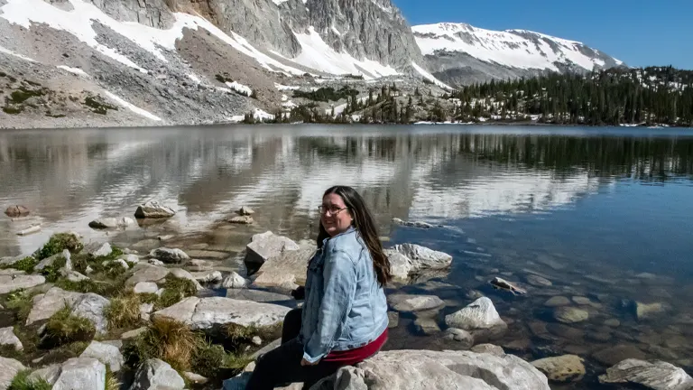 a tranquil scene at Medicine Bow–Routt National Forest, featuring a person sitting on rocks by a serene lake surrounded by snow-capped mountains
