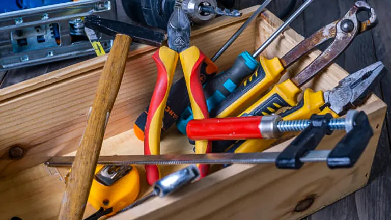 A variety of hand tools, including hammers, pliers, and screwdrivers, scattered inside a wooden toolbox.