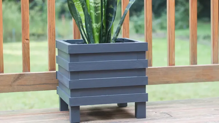 A completed blue wooden planter box with a plant inside, located on a porch railing.