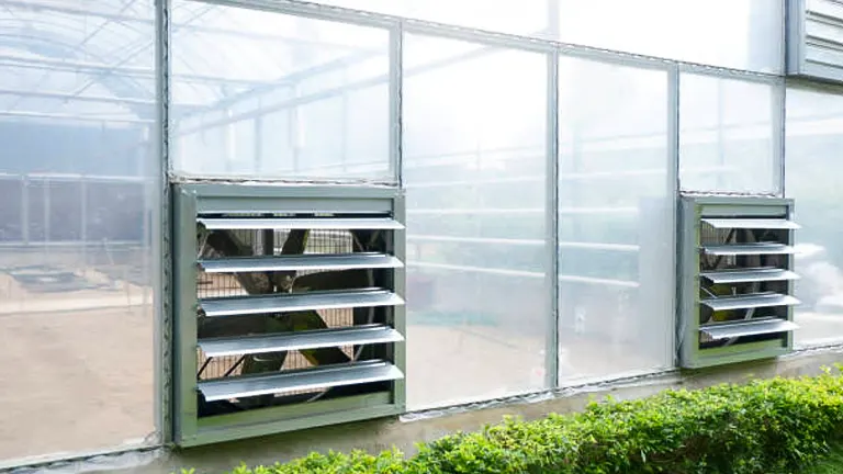 Greenhouse shelves with seed trays visible through large windows in a bright, misty setting.