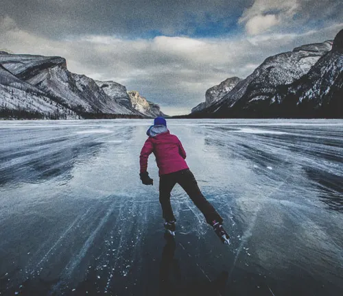Person ice skating on a frozen lake surrounded by mountains