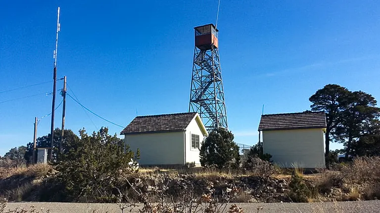 Metal lookout tower with two small buildings and a utility pole against a clear blue sky