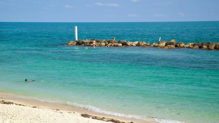 People enjoying the clear turquoise waters near a rocky barrier at Fort Zachary Taylor Historic State Park