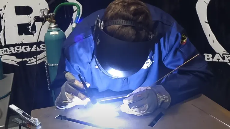Person in protective gear welding a metal piece with a Deca Miga 215 Multiprocess Welder