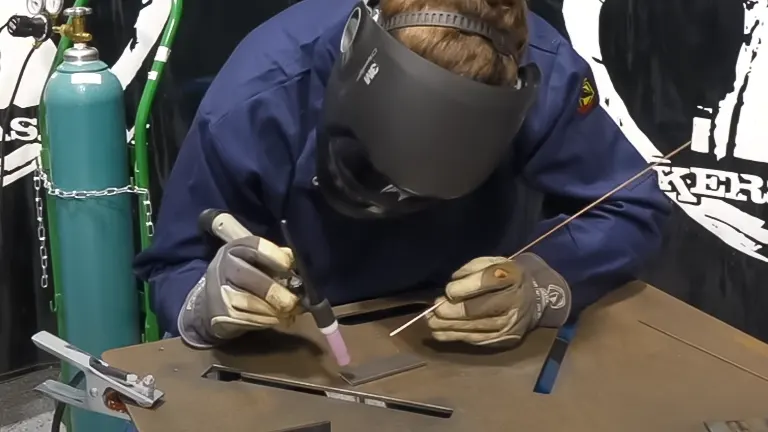 Person welding a metal piece with a Deca Miga 215 Multiprocess Welder, wearing safety gear