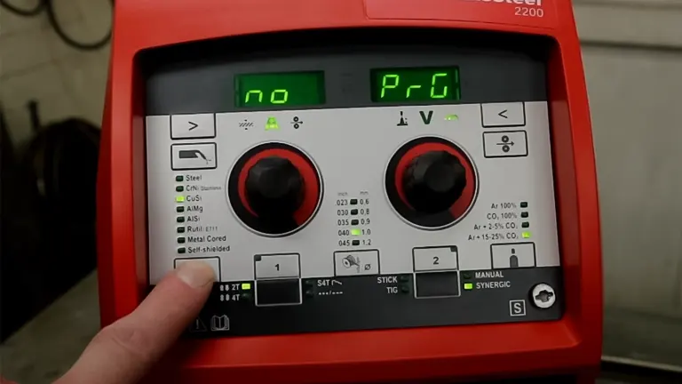 Close-up of a red welding machine’s control panel displaying settings, with a hand adjusting a knob