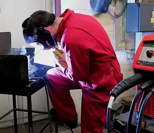 Person welding in a workshop with a red welding machine