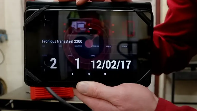 Person holding a tablet displaying data from a Fronius TransSteel 2200 machine