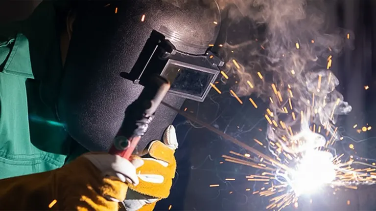 Welder in protective gear welding a pipe, with sparks flying