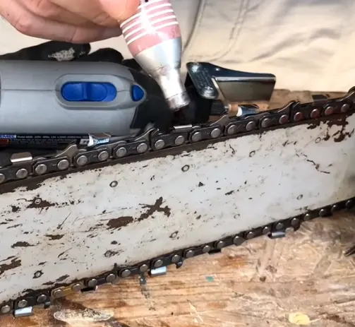 Dremel tool with a sharpening guide attached, sharpening a chainsaw blade