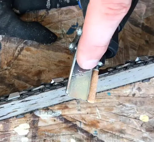 Person aligning a metal guide parallel to a chainsaw tooth, with the 30-degree line aligned with the chain