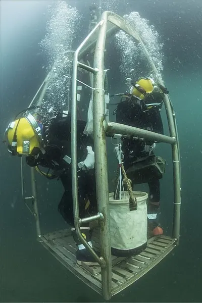 Underwater welder working within a metal cage in murky waters