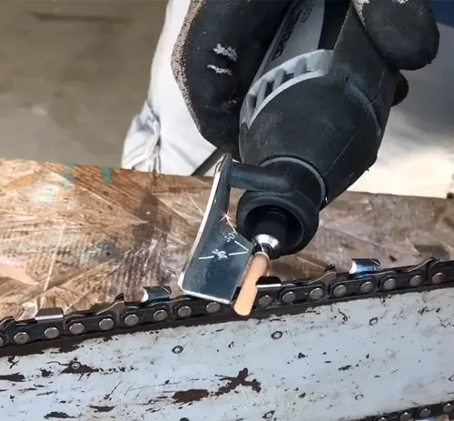 Person wearing safety gloves sharpening a chainsaw blade on a wooden surface