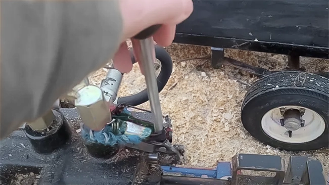 A person's hand engages the control valve on a blue hydraulic log splitter near a vehicle's tire.