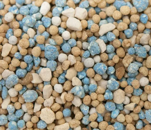 Close-up of slow-release fertilizer granules in a blend of blues, whites, and browns, indicating the variety of nutrients formulated for sustained release to plants.