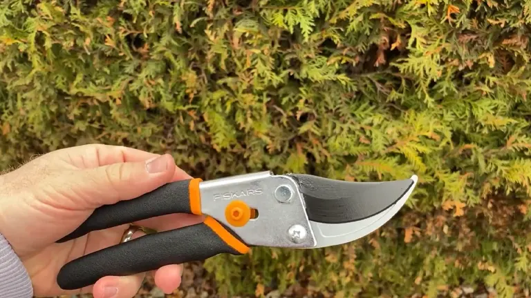 A hand holding a pair of Fiskars Pruning Shears open, with a green shrubbery background.