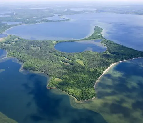 Aerial view of a verdant peninsula with a distinctive boot shape, surrounded by the blue waters of a vast lake.