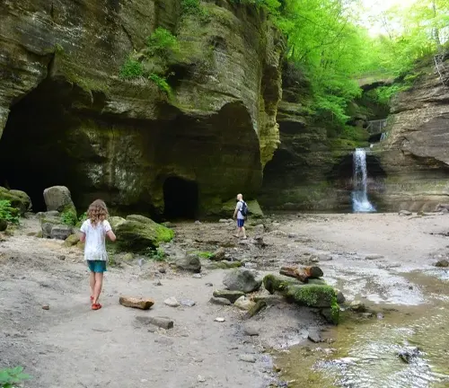 A child and adults exploring a forest with a waterfall and caves.
