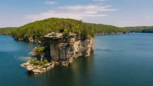 Aerial view of Summersville Lake State Park showcasing the expansive calm waters with a rugged, tree-covered cliff formation jutting into the lake
