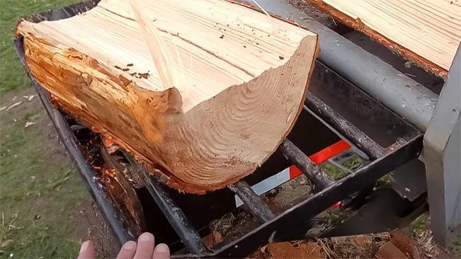 A close-up of a log splitter with a large, freshly split log positioned on the splitting bed, outdoors.