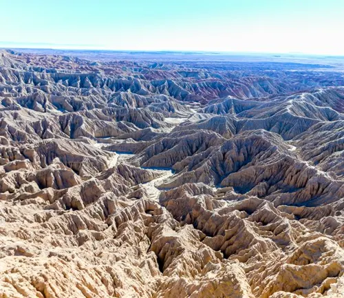 An expansive view of rugged desert canyons with layered rock formations, under a clear blue sky.

