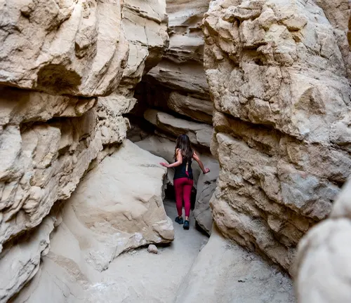 A person in red pants exploring a narrow crevice between large sandstone rocks.