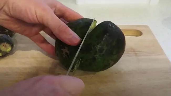 A hand slicing an avocado in half on a wooden cutting board