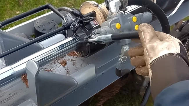 A gloved hand operates the control lever of a log splitter, with a focus on the machine's hydraulic arm and control panel.
