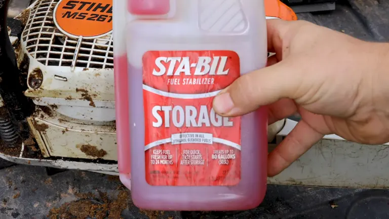 Hand holding a bottle of STA-BIL Fuel Stabilizer in front of a used STIHL MS 250 engine, indicating maintenance process.
