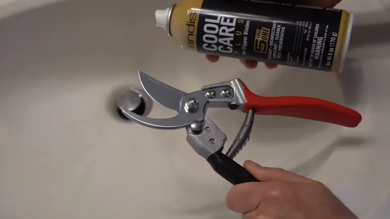 A hand holding a pair of garden shears with an Andis Cool Care spray can in the background, positioned on a white surface.