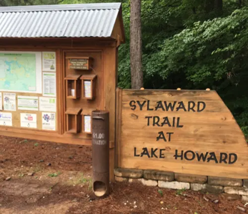 A wooden trailhead information board and map for Sylaward Trail at Lake Howard, surrounded by trees, with a large wooden sign in front.