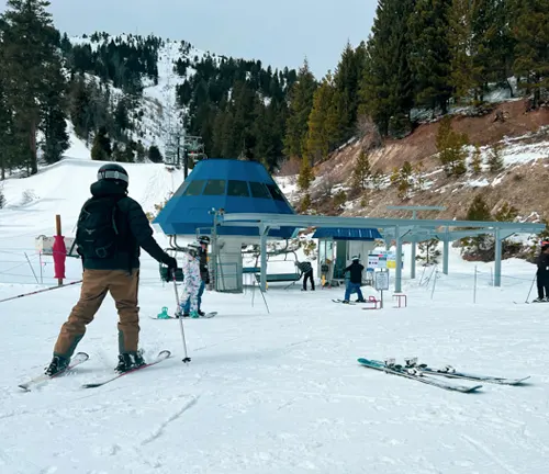 Skiers at the base of a snowy slope with a ski lift station ahead, ready to ascend the mountain for their next run.