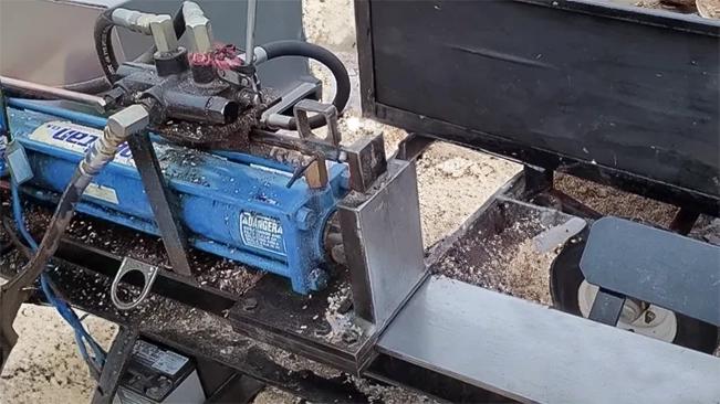 Close-up of a blue hydraulic log splitter with sawdust scattered around the mechanism.