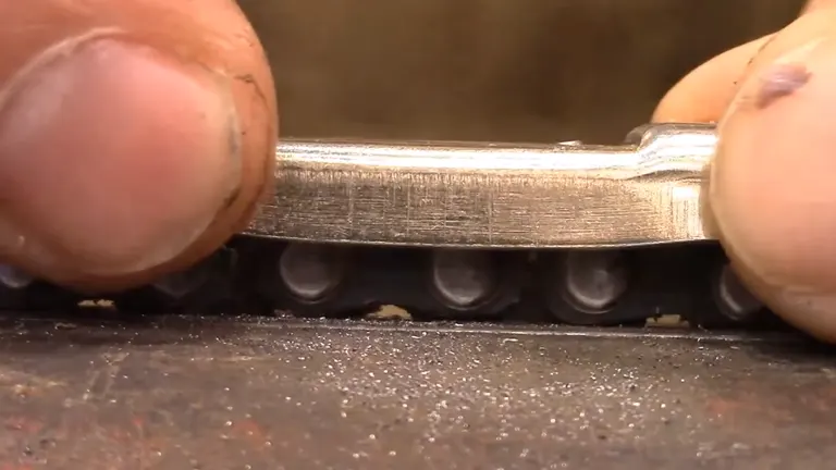 Close-up of hands using a file to sharpen each tooth of a saw blade