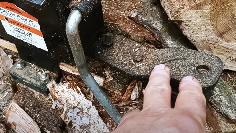 Hand touching a part of the Champion 90720 7-Ton Log Splitter near wood debris and a warning label